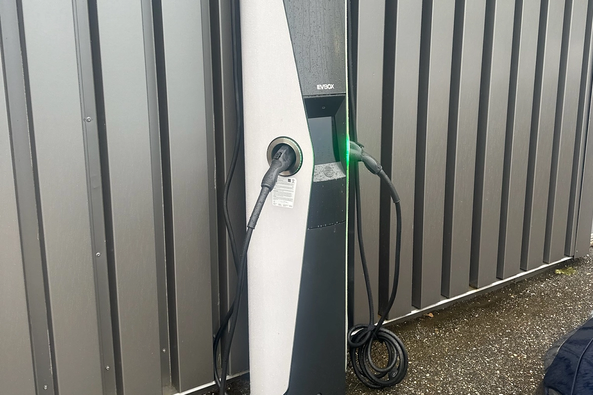 Installed EVBox electric vehicle charging station mounted on a gray metal wall, charging cable connected and glowing green
