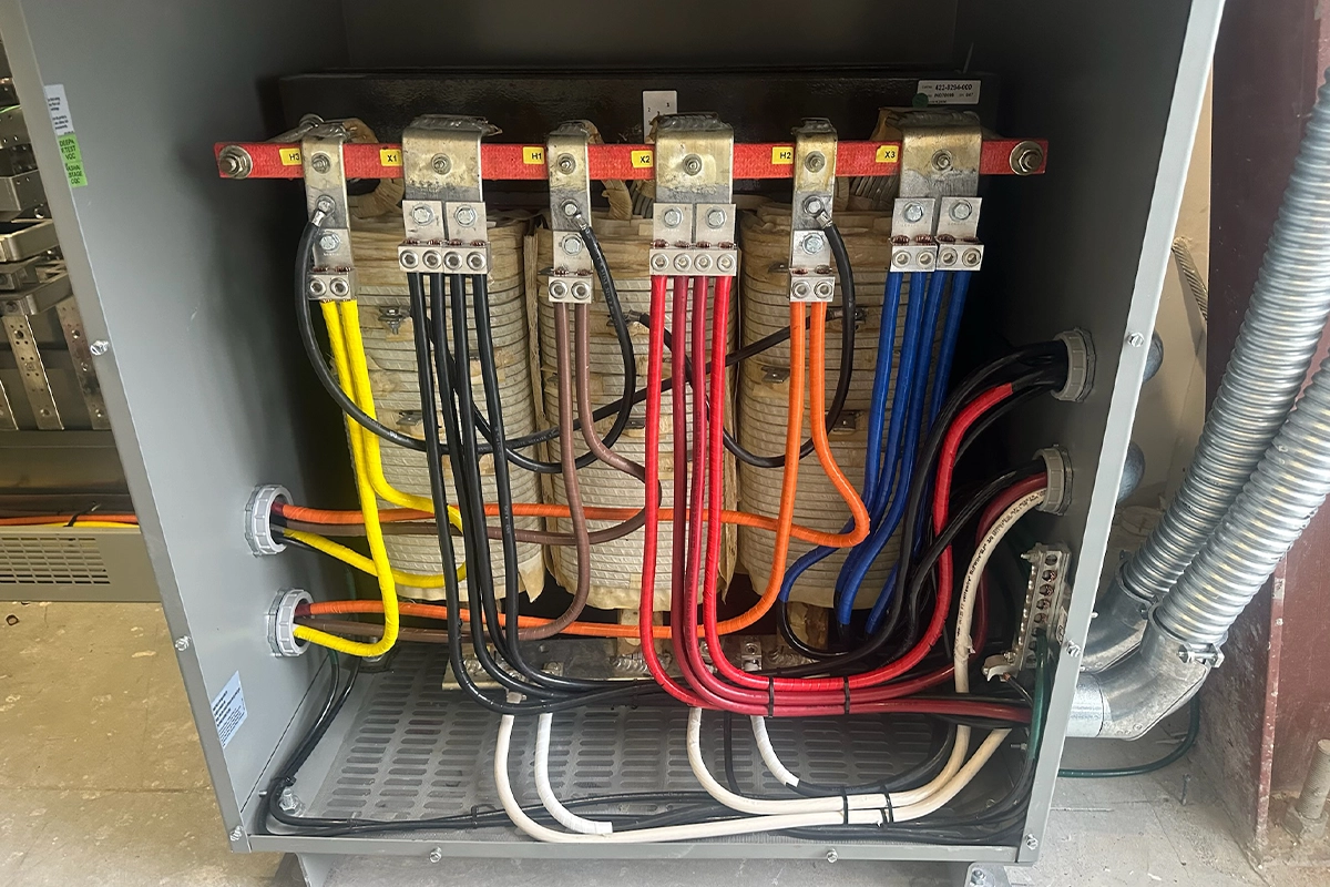 Electrical transformer cabinet with color-coded wiring connections and labeled terminals for power distribution.